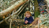 Small boy with curly ginger hair, wearing purple fleece playing with stick amidst tree branches, Craigivinean Forest, Dunkeld