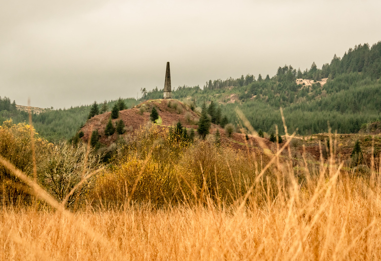 A stone monument through the grass on a hill 