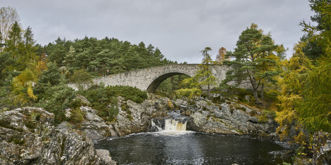 A river with a small ledge under an old stone bridge in autumn,