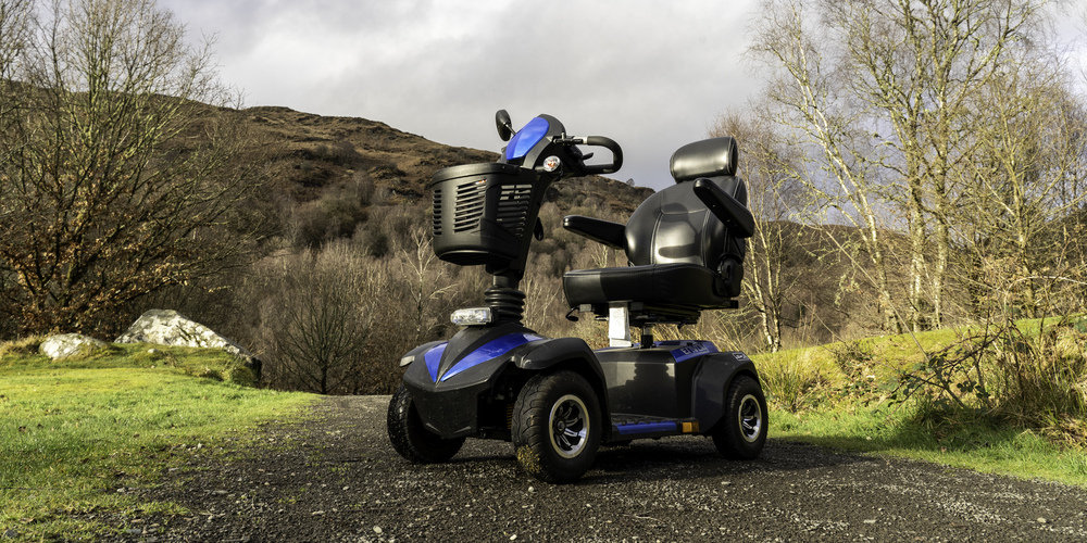 A blue mobility scooter on a gravel path with a mountain behind