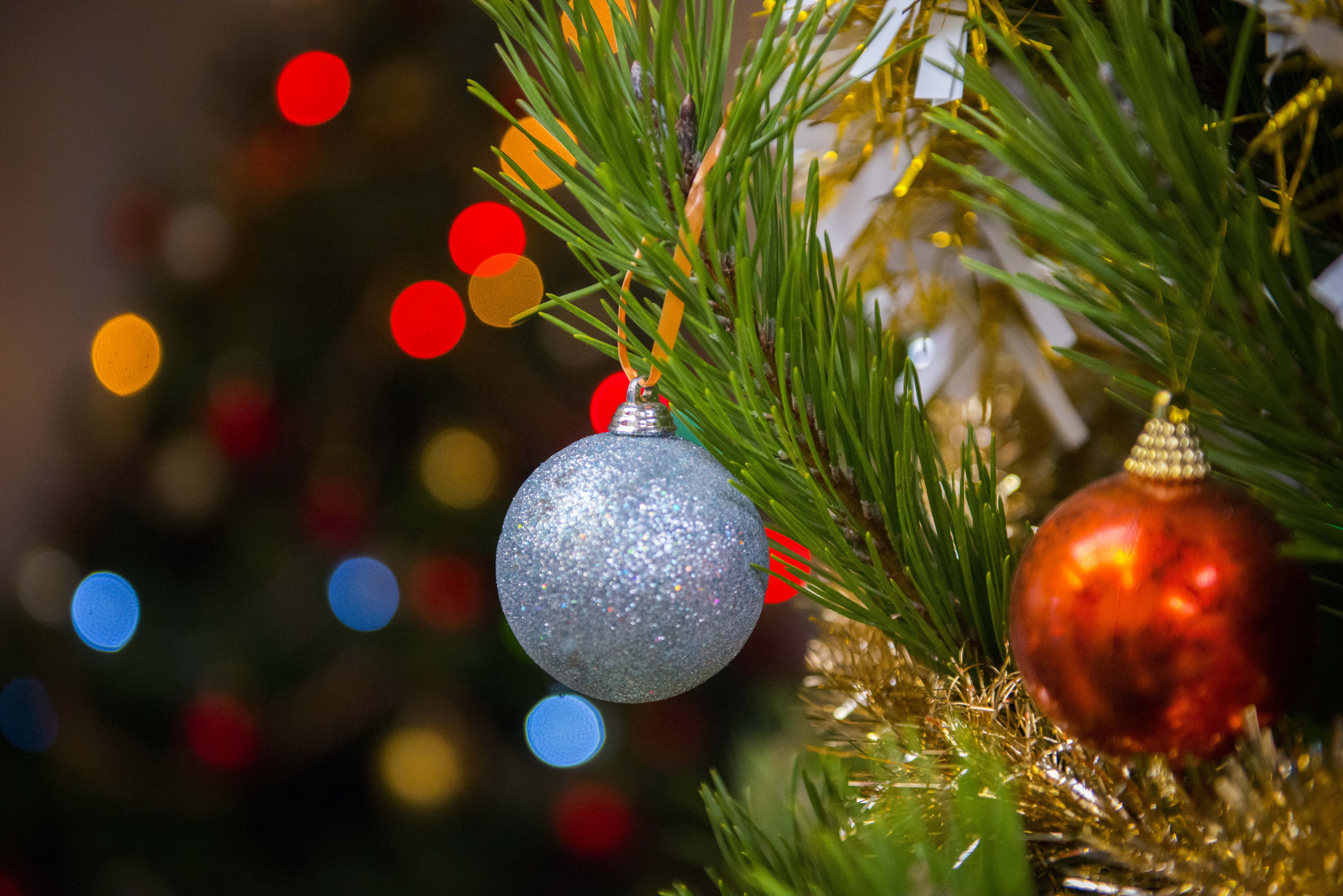 Close up of a sparkly blue Christmas bauble hanging from a Christmas tree. There are colourful lights in the background. 
