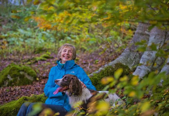An elderly woman sits with her dog in an autumn forest 