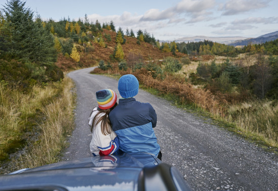 Two people leaning on car bonnet looking towards forest