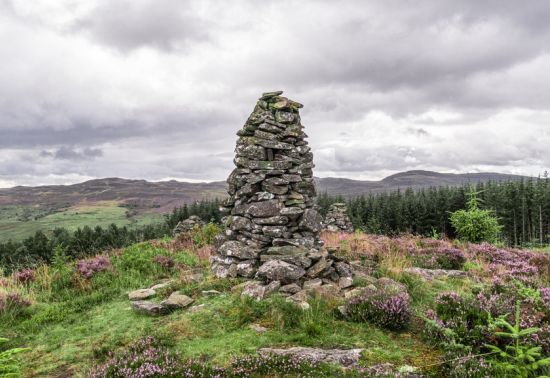a stone carin on the top of a hill with heather