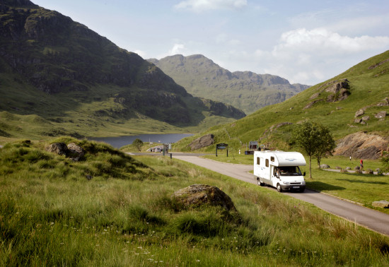 Campervan driving on small singletrack road amongst lush green hillsides