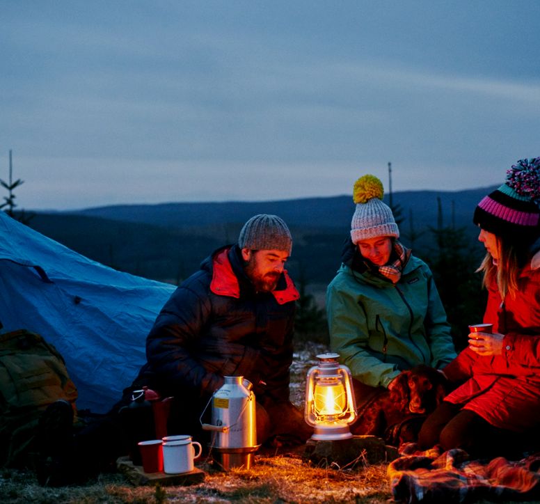 Three people gathered around a camping stove at dusk