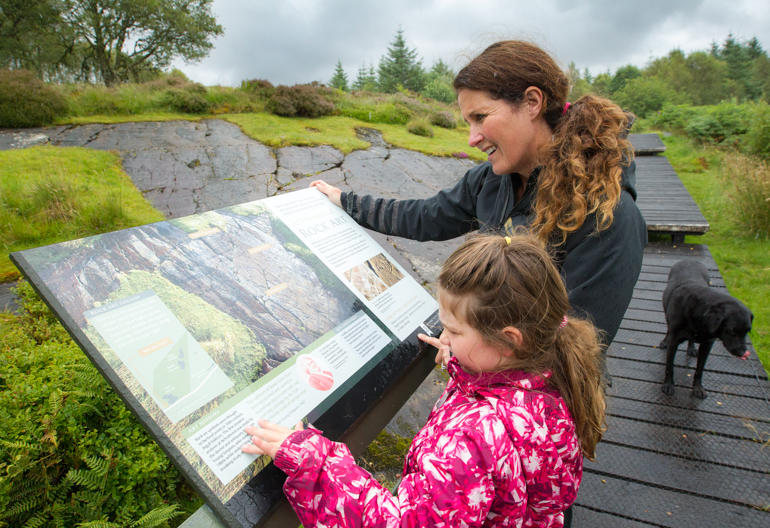 Woman and young girl in pink look at Rock Art interpretation board, Achnabreac