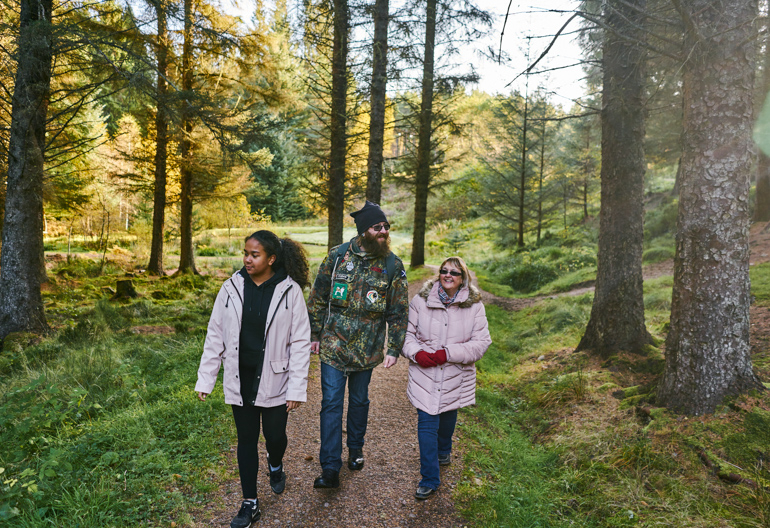 A man, woman and teenage girl walking along tree lined woodland path, Aldie Burn forest, near Tain