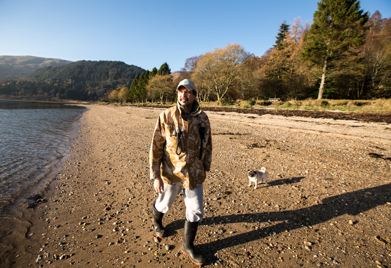 Man with dog walks along shore of Loch Long, with sweep of forests in background, Ardentinny, Argyll Forest Park