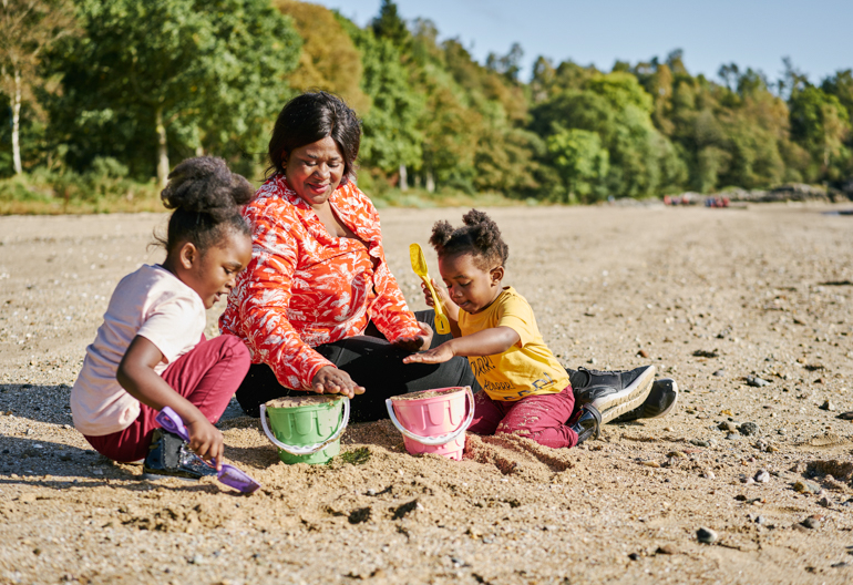 Woman and two young girls sitting on beach making sand castles at Ardentinny, on the shore of Loch Long
