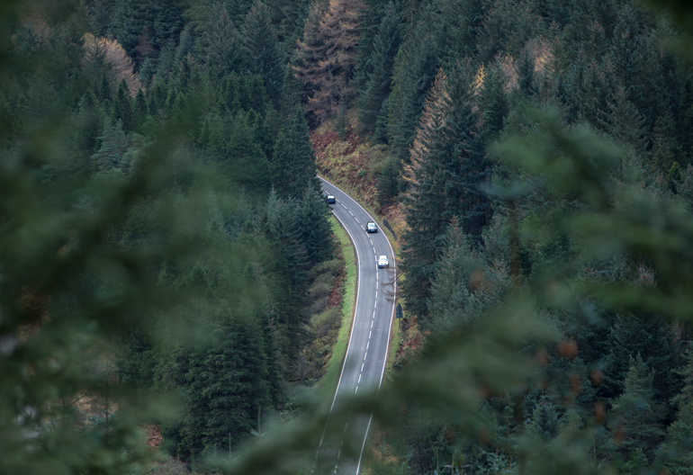 Aerial view of motorway though dense forest of conifers, Ardgartan, Argyll Forest Park