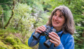 Woman in blue top holds binoculars in hand, Balnain, near Loch Ness