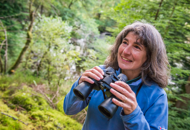 Woman in blue top holds binoculars in hand, Balnain, near Loch Ness