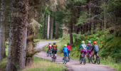 Rear view of group of women and small boys on mountain bikes ride on cycle path, Balnain near Loch Ness