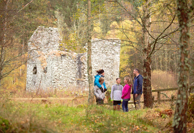 Man, woman and three children standing under trees with Cardrona Tower in background, Cardrona Forest, near Peebles