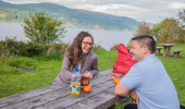Woman and man sit at picnic bench with a snack, at Change House, south side shore of Loch Ness
