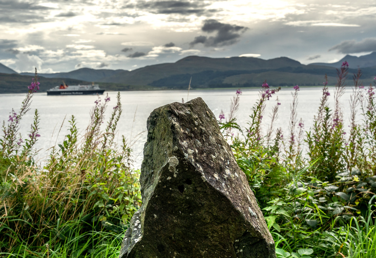 A stone wall with a single stone structure and the Isle of Mull behind it