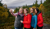 Two women and two teenage girls take a selfie photo at Contin, near Strathpeffer, with woodland and Strathconon hills in distance