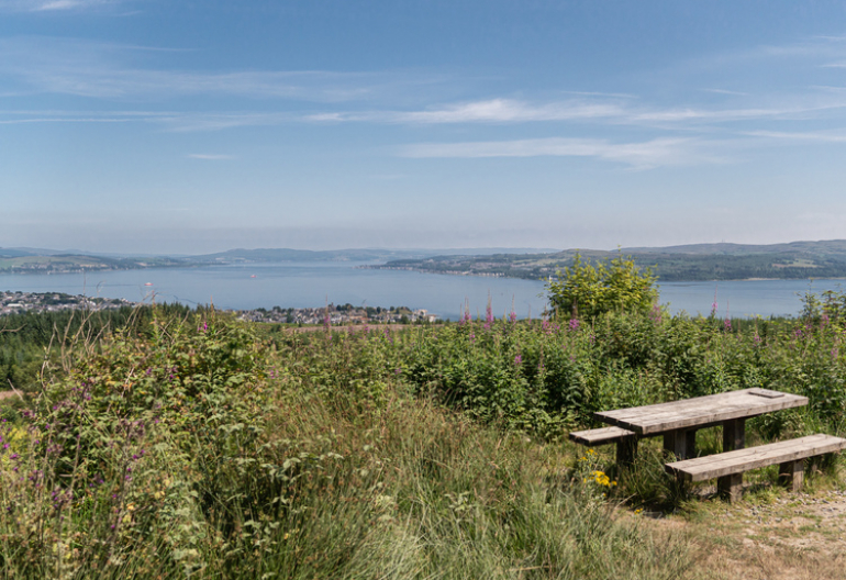 A picnic table on the edge of a cliff with a town and sea below