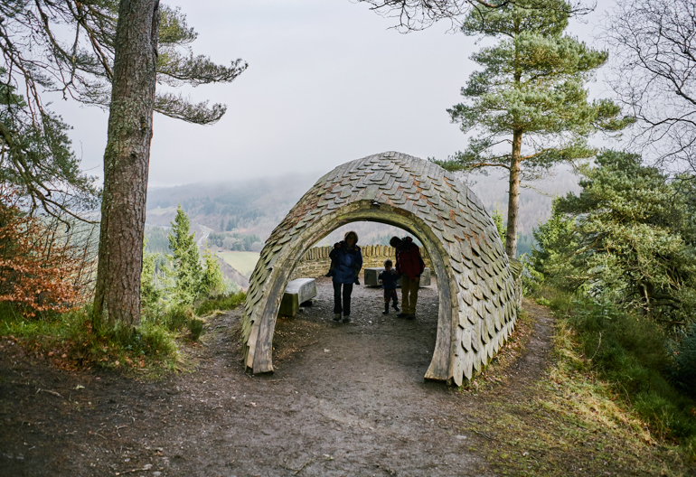 Family of two adults and two children inside Pine Cone Point viewing shelter, Craigvinean Forest, Dunkeld