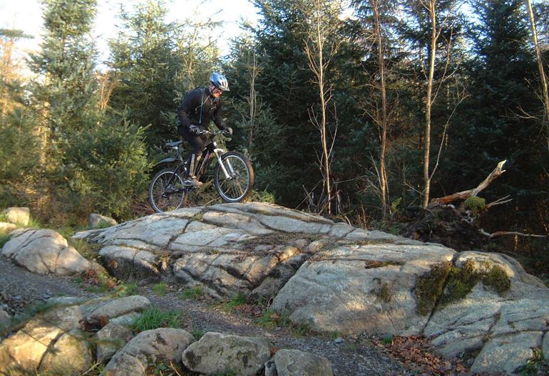 A man with a blue helmet rides his mountain bike over a large rock surface 
