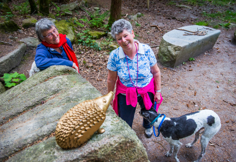 Two women look at golden hedgehog sculpture on top of boulder, Dalbeattie Forest, near Dumfries