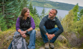  Male and female walker sitting on rock consulting map, with Loch Ness behind them,Farigaig, near Inverfarigaig
