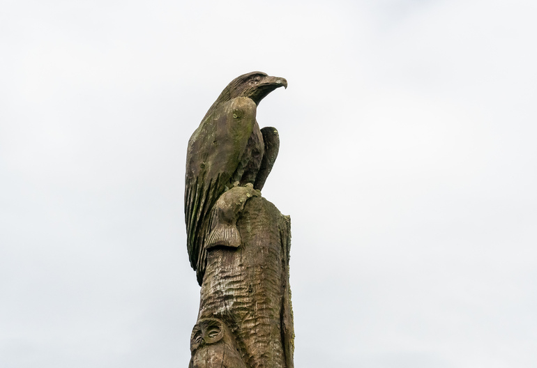 A wooden totem pole with an eagle holding a fish with an owl under it.