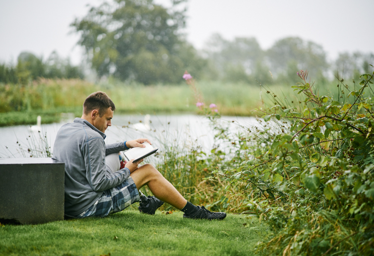 A man sits on grass next to a pond