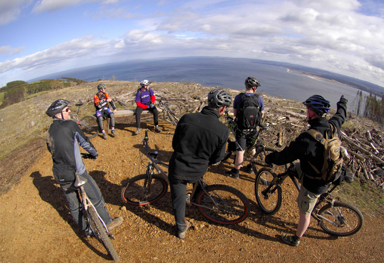 A group of mountain bikers look out to sea from a hilltop