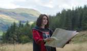 A woman reads a map in front of conifer woodland