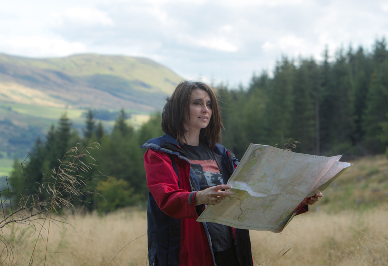 A woman reads a map in front of conifer woodland