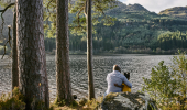 A father and daughter sit on rocks looking out over a loch