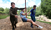Two children push another on a zip-line swing in an adventure playground.