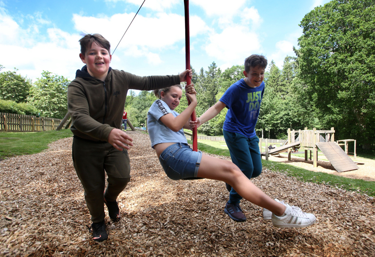 Two children push another on a zip-line swing in an adventure playground.