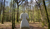 Strange stone sculpture of a woman's dress in pale stone placed in a forest.
