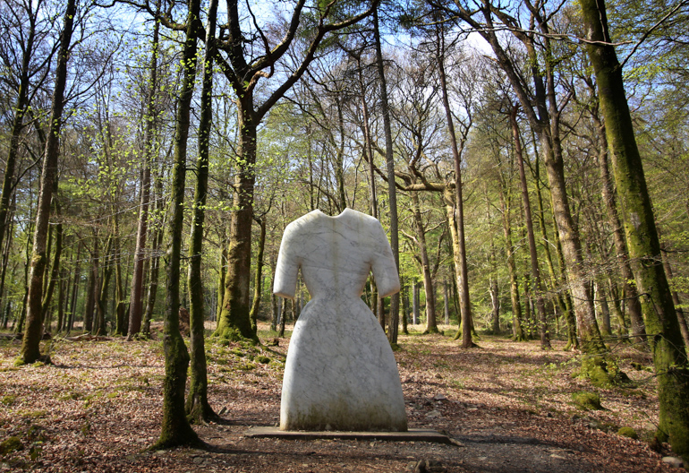 Strange stone sculpture of a woman's dress in pale stone placed in a forest.