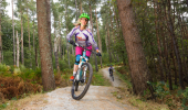 Woman on a mountain bike trail riding between trees in an open forest.