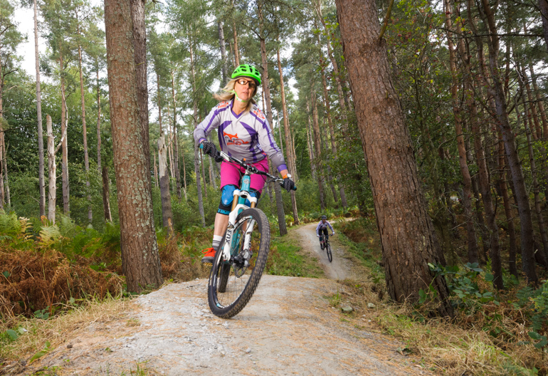 Woman on a mountain bike trail riding between trees in an open forest.