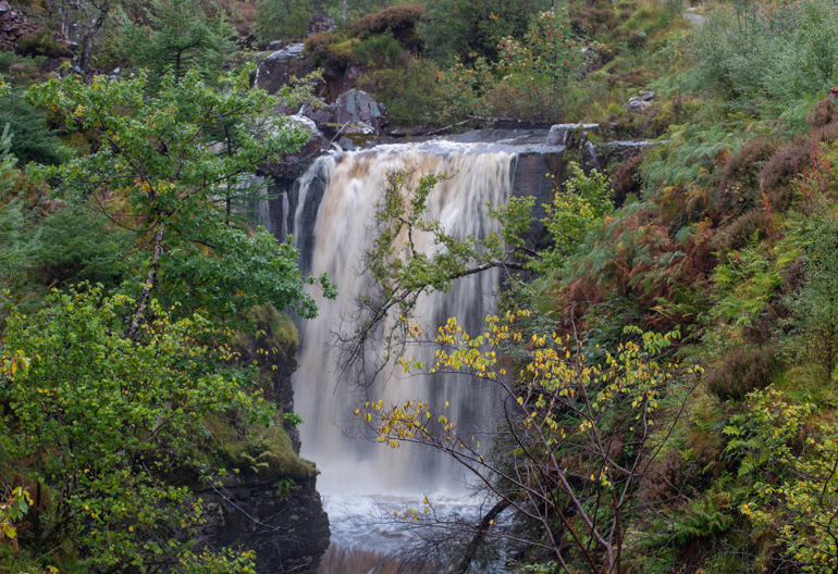 A large waterfall surrounded by broadleaf trees in autumn