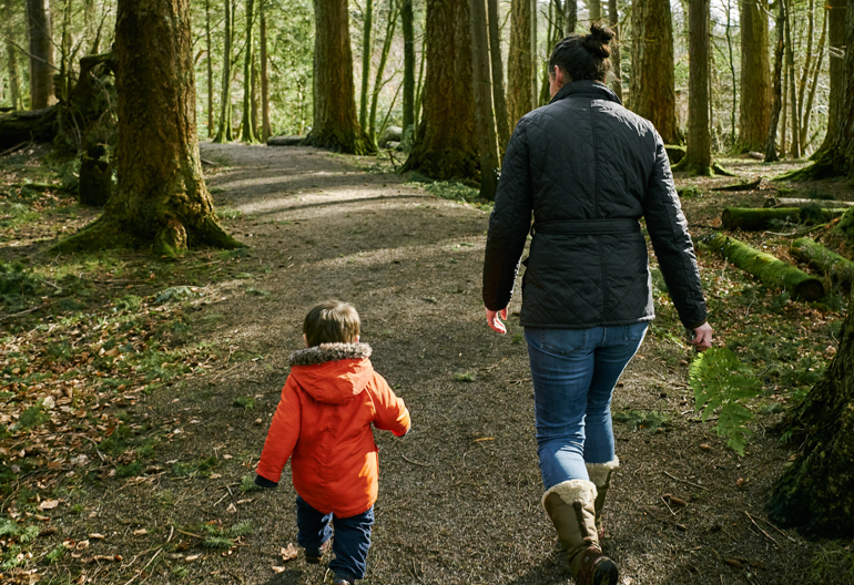 A woman and a small boy walk along a wide woodland path