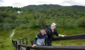 Two boys climb a wooden staircase up a grassy hillside from a lush woodland
