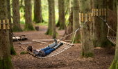 A boy lies in a hammock strung between two trees in a forest