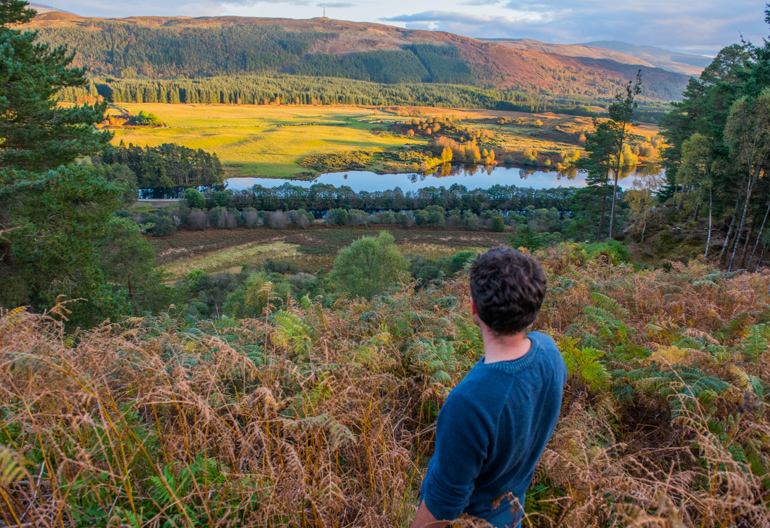 Rear view of man at Torr Dhuin looking across panorama as evening sun spills across River Oich and surrounding mountain range, near Fort Augustus