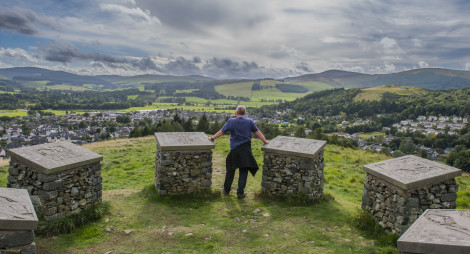 Man stands at sculptures on Pirn Hill Fort Trail, overlooking Innerleithen, Caberston