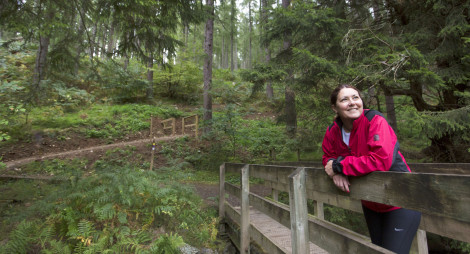 Woman in red jacket leans on wooden bridge, surrounded by trees, Cardrona Forest, near Peebles