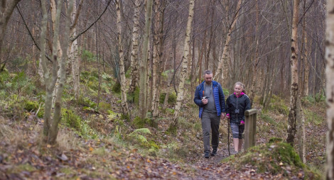 Man in blue jacket walking beside young girl carrying a stick on woodland path, Glenkinnon, near Clovenford