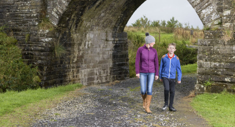 A woman and a boy walk along a wide path beneath a stone archway