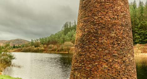 A brick structure next to a loch with trees along the bank