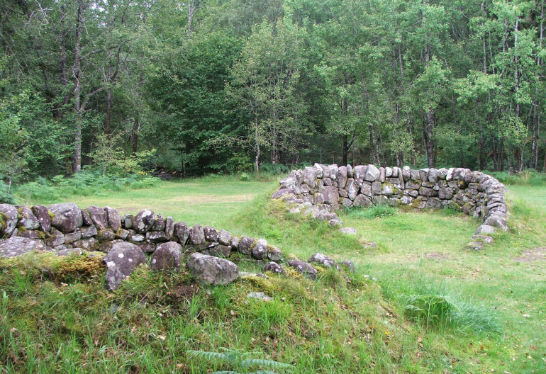 Rough stone shelters on a grassy field surrounded by tall green trees